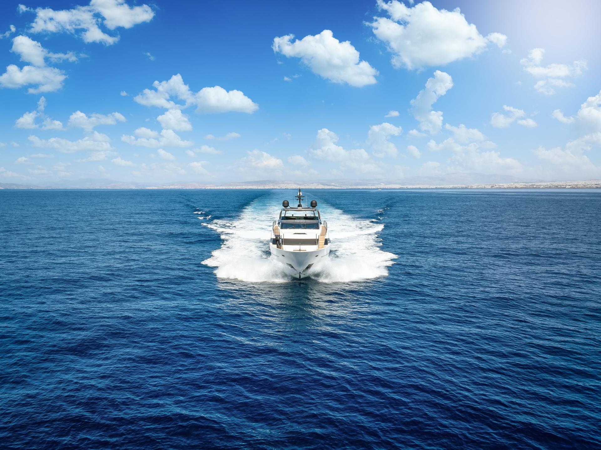 (Selective focus) Stunning sunrise during a cloudy day with a rock in the foreground and a luxury yacht sailing on a calm water in the distance. Golfo Aranci, Sardinia, Italy.
